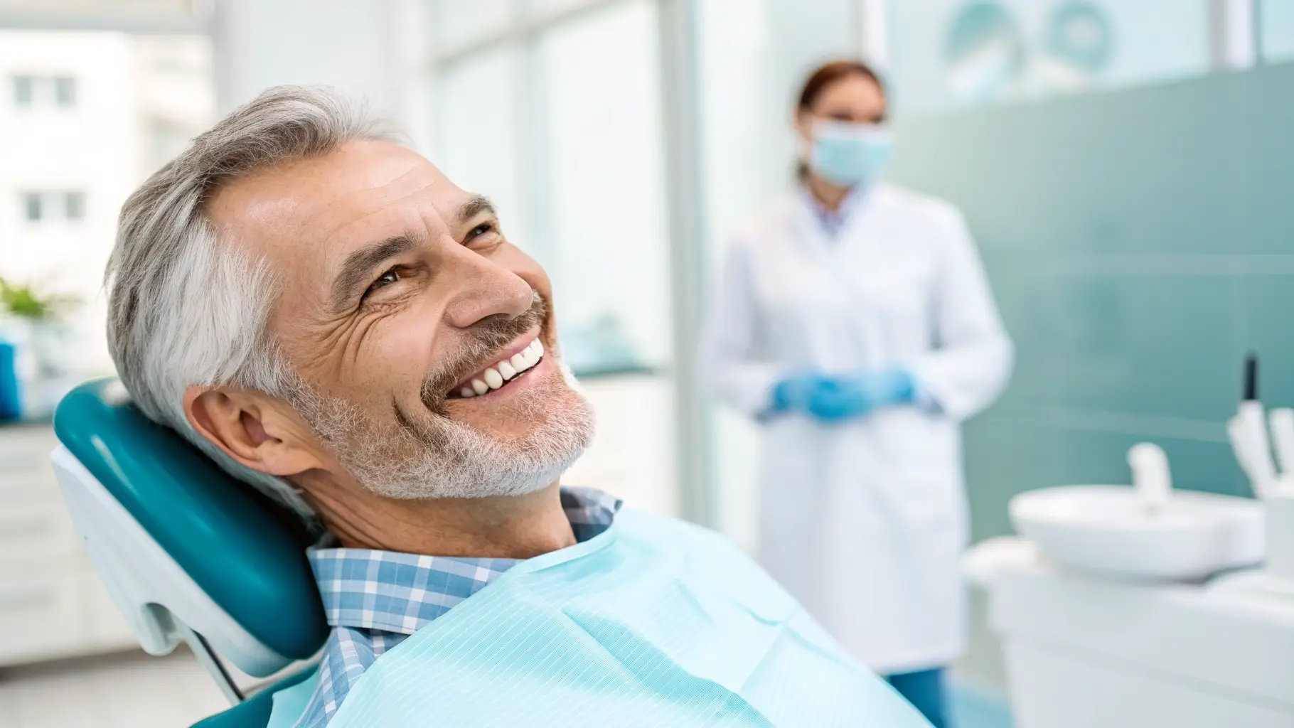 Smiling woman in a dental chair with a dentist in the background, soft focus, professional dental clinic setting.